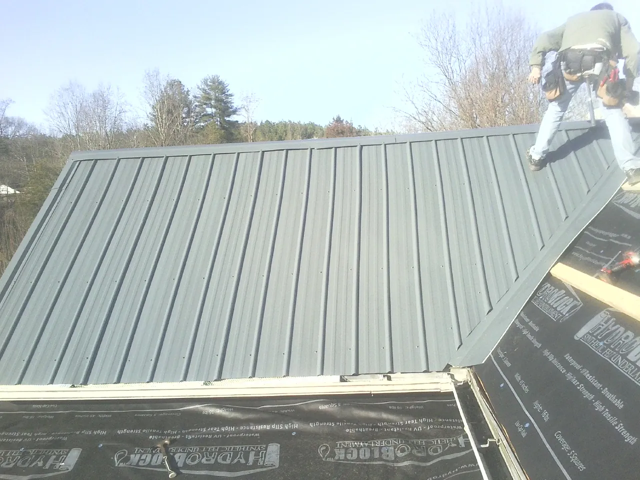 Crew installing dark green standing seam panels over synthetic underlayment in Lorida