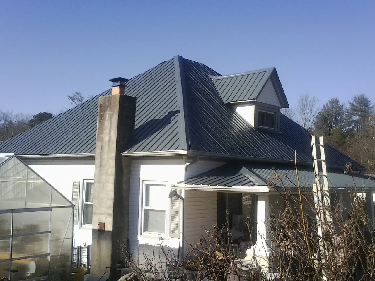 Dark blue standing seam metal roof on a white farmhouse with dormer — Slate & Tile Roof Repair by Roofing Brothers in Lorida