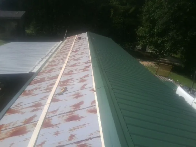 Old rusted panels beside newly installed green metal roofing — Wind Damage Roof Repair by Roofing Brothers in Lorida