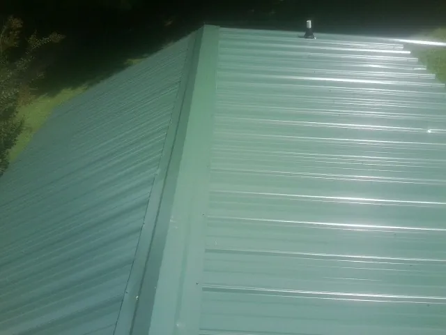 New green metal panels meeting at the ridge of a roof — Flat Roof Repair work by our crew in Lorida