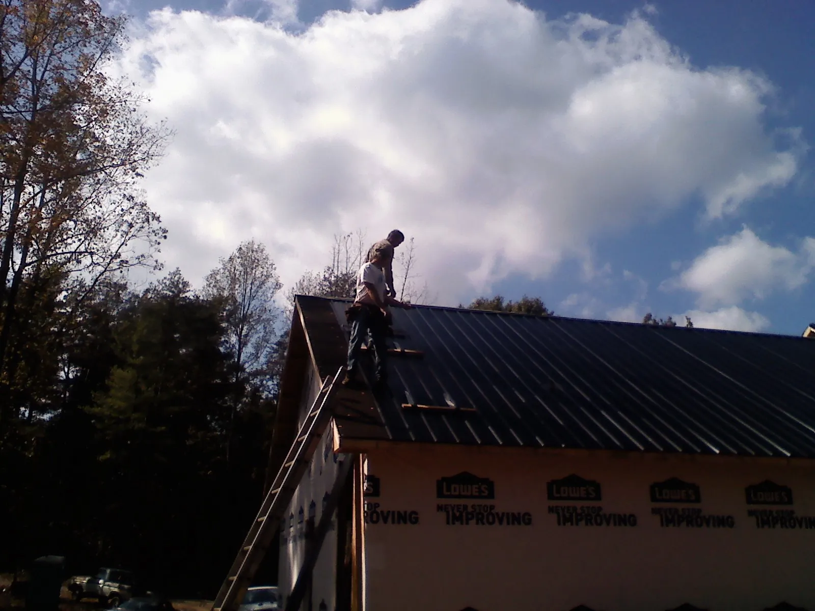 Roofer fastening dark metal panels high against a cloudy sky, from a Roof Inspection job in Lorida